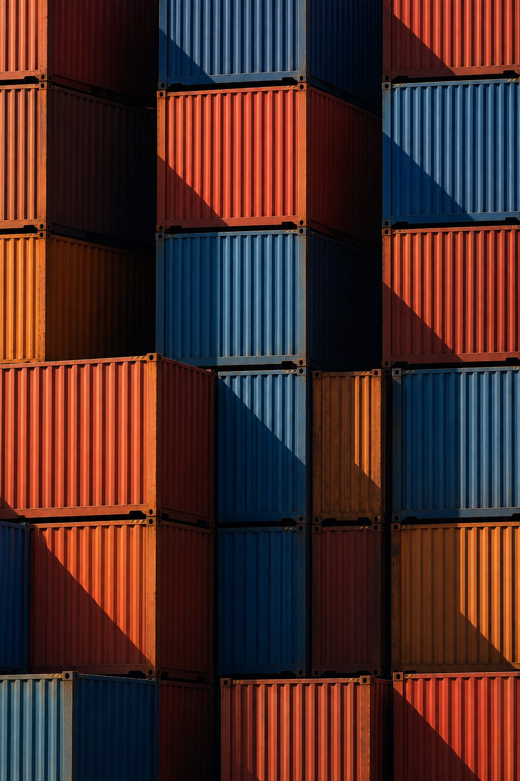 Stacked shipping containers filling the frame, hard diagonal shadows across them